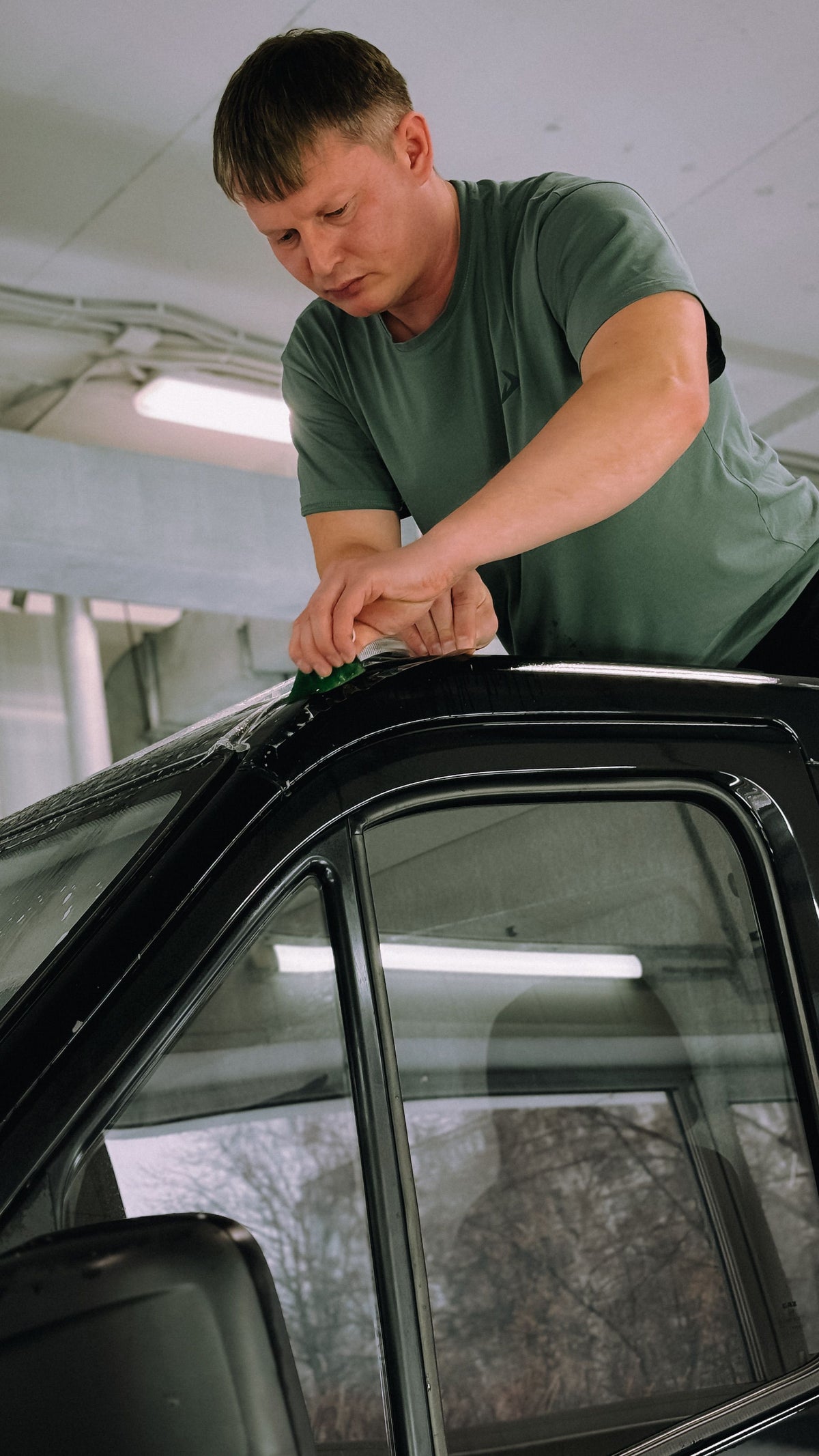 Person working with window tint film on car glass in a workshop. Stock installation photo by Bulat843; tools and installation service are not included.